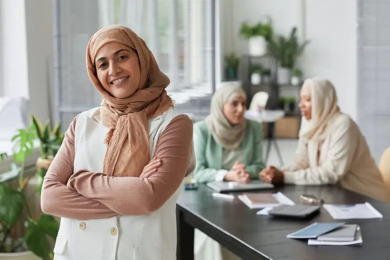 Une professionnelle souriante au premier plan, ses collègues en réunion derrière elle